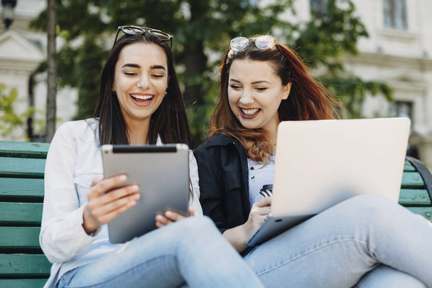 Duas adoráveis mulher rindo enquanto olha para uma tela de tablet enquanto
 - Foto, Imagem