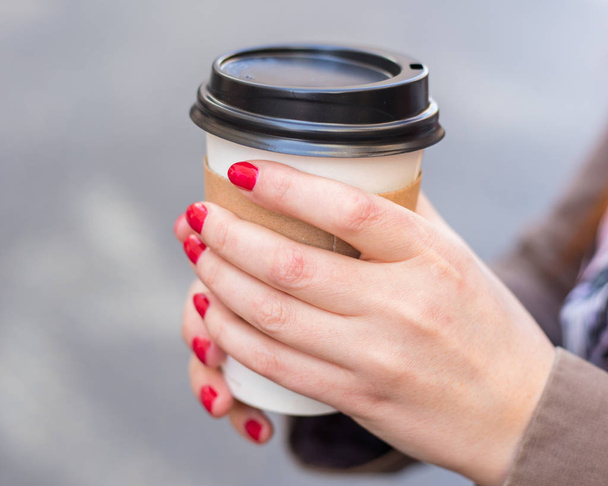 Donna che tiene una tazza di caffe 'sulla strada sfocata. Pomeriggio soleggiato di primavera. Manicure rossa
 - Foto, immagini