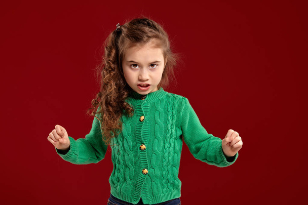 Portrait of a little brunette girl with a long, curly hair posing against a red background. - Photo, Image