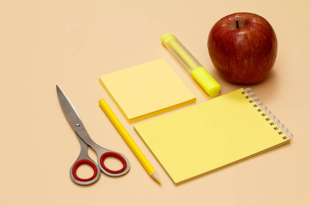 Des fournitures scolaires. Ciseaux, pomme, crayon, cahier, feutre et papier à lettres sur fond beige
. - Photo, image