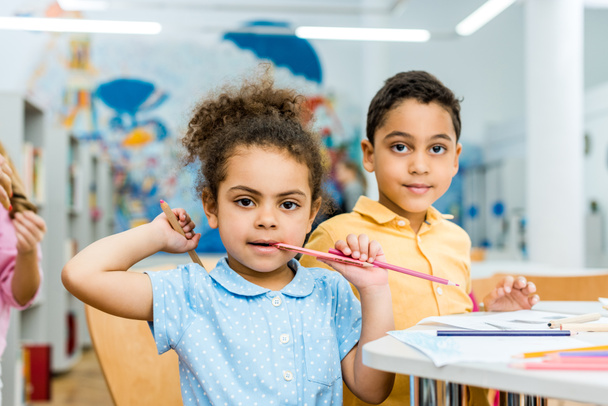 selectieve focus van leuke Afro-Amerikaanse kind bijten potlood in de buurt van schattig kind  - Foto, afbeelding