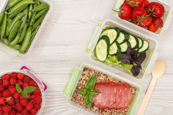 Plastic meal prep containers with boiled buckwheat porridge and slices of meat, fresh vegetables and berries. - Photo, Image