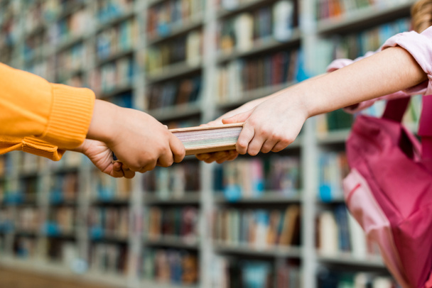 oříznutý pohled na děti tahání knih při stání v knihovně  - Fotografie, Obrázek