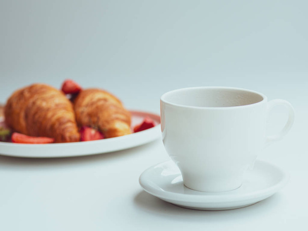 Kesäaamiainen kahdella croissantilla, tuoreilla mansikoilla ja kupillisella kahvia. lähikuva valkoisella pohjalla
 - Valokuva, kuva