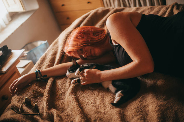 redhead woman lying on the bed stroking a kitten - Foto, imagen