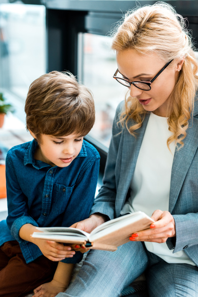 selective focus of woman in glasses reading book with cute kid  - Foto, Bild