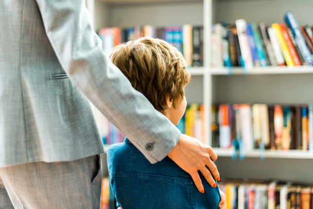 cropped view of woman standing with kid in library  - Foto, imagen