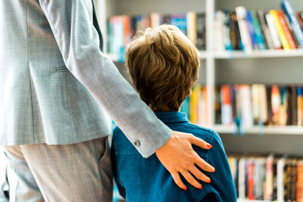 visão traseira da criança de pé com a mulher na biblioteca
  - Foto, Imagem