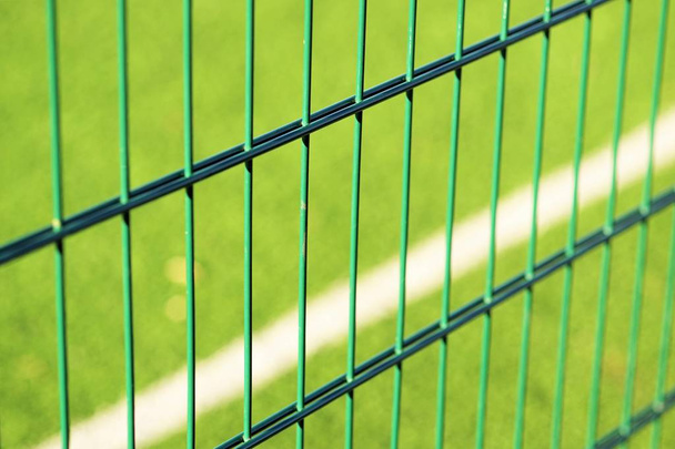 ミニサッカーをプレイするための芝生のフィールドの背景に緑のフェンスのグリッド - 写真・画像