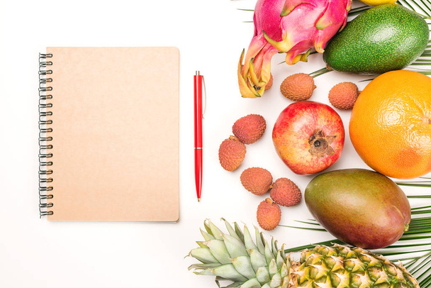 Egzotyczne owoce, jedzenie, zdrowe odżywianie i koncepcja wegetariańska. Tropikalne owoce i Notatnik na białym stole.  - Zdjęcie, obraz