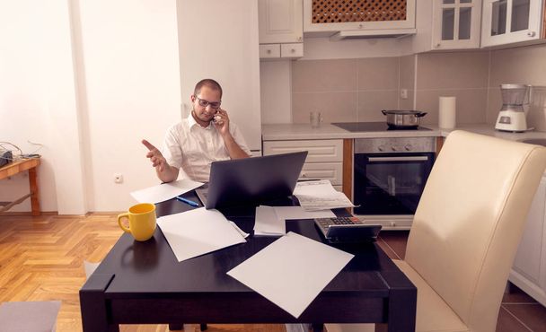 Οικονομικός άνθρωπος που εργάζεται και μιλάει στο τηλέφωνό του στο σπίτι - Φωτογραφία, εικόνα
