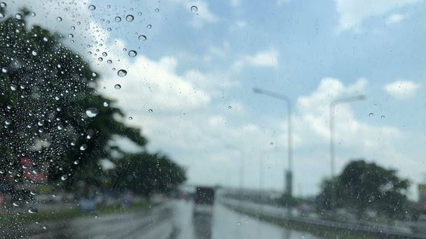 Yağmur damlaları araba ön cam, bulanık ışık arka plan, yağmurlu bir gün şehirde trafik, renkli bokeh. - Fotoğraf, Görsel