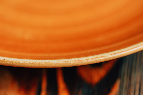 Orange ceramic plate on a wooden stand. Texture of burnt wood surface. - Photo, Image