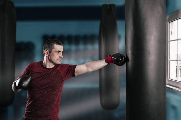young short-haired man is training in a gym with a punching bag. - Фото, изображение