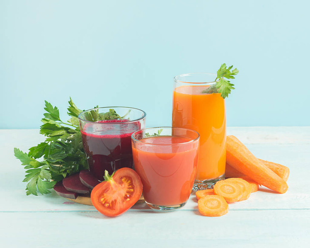 Batidos de jugo fresco de una variedad de verduras remolacha manzana zanahoria tomates en vasos sobre fondo azul de madera
. - Foto, imagen