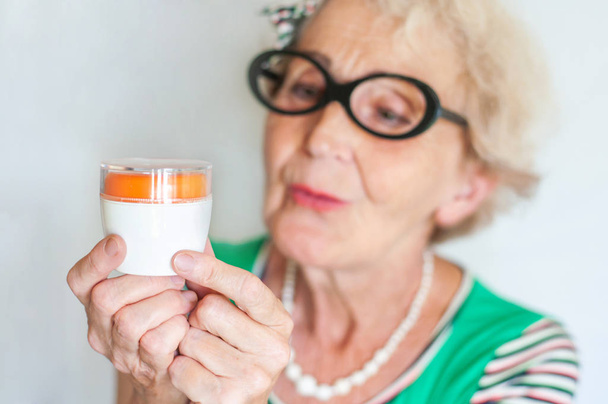 Mujer hipster arrugado maduro en gafas divertidas examina un frasco de crema facial. El cuidado de la piel para las mujeres 60-70 años. Mujeres Salud
 - Foto, imagen