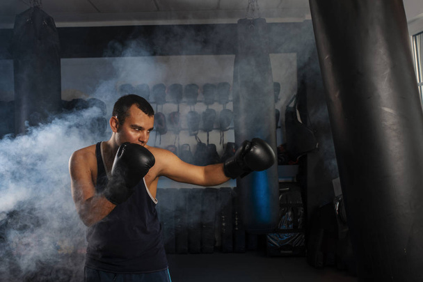 jeune homme aux cheveux courts s'entraîne dans une salle de gym avec un sac de boxe
. - Photo, image