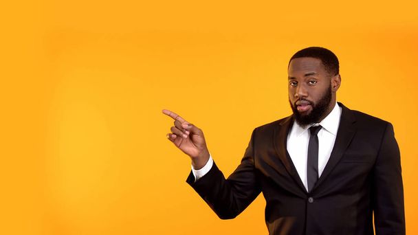 Black male in business suit pointing with finger left, looking to cam, template - Foto, Bild