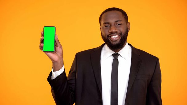 Φιλικός όμορφος Αφρο-Αμερικανός άντρας με κοστούμι που δείχνει το τηλέφωνο, πρότυπο - Φωτογραφία, εικόνα