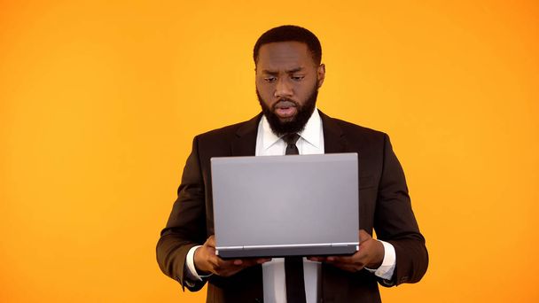 Αφρικάνικο-αμερικανικό αρσενικό διαβάζοντας ειδήσεις για το laptop και συνοφρυωμένο, ντροπιαστικό ειδήσεις - Φωτογραφία, εικόνα