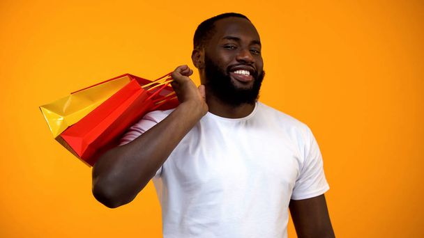 Afro-American man holding shopping bags and smiling at camera, season discount - Foto, Bild
