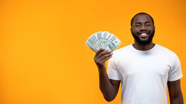 Smiling African-American man showing bunch of dollars, template for text, ad - Photo, image