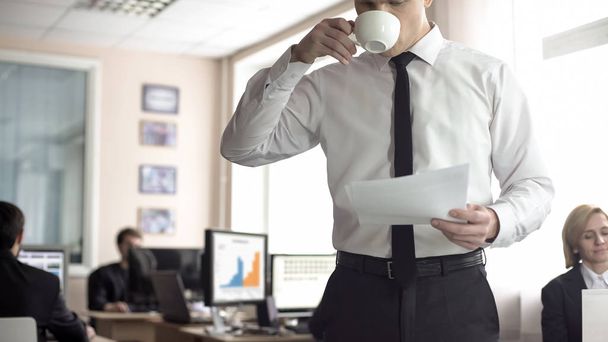 männlicher Manager blättert in Unterlagen und trinkt Kaffee, Büroarbeit - Foto, Bild