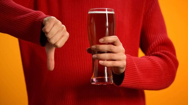 Woman holding glass of beer showing thumbs down, drunk driving danger, alcohol - Zdjęcie, obraz