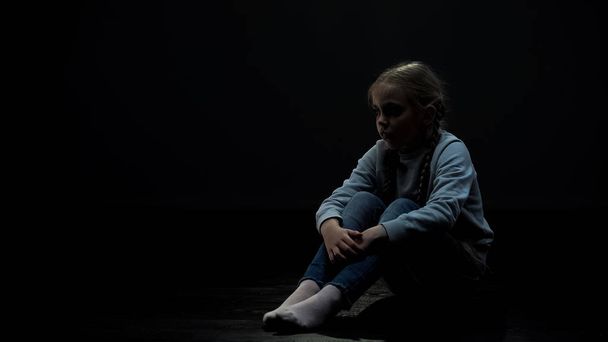 Upset little girl sitting in dark room alone, fear and problems, orphan kid - Fotó, kép