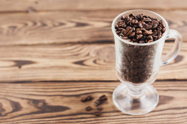 Csomó sült kávébab átlátszó üveg forralt bor fogantyúval és lábbal mellett szétszórt szemek a régi fa rusztikus barna deszka - Fotó, kép