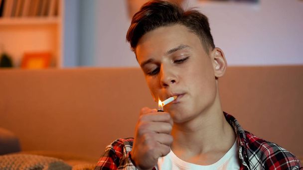 Teenager boy lightning and smoking cigarette, harmful unhealthy habit, cancer - Photo, image