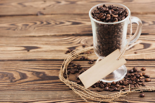 Sok sült kávébab átlátszó üveg forralt bor téglalap üres papírt a kötél közelében szétszórt kávébab a régi fa rusztikus barna deszka - Fotó, kép