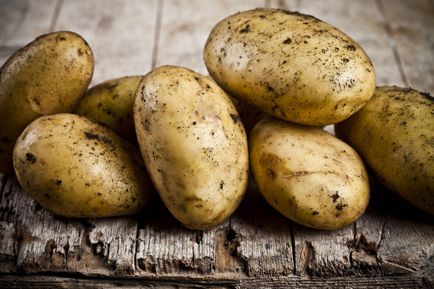 Newly harvested dirty potatoes heap on rustic wooden background. - Zdjęcie, obraz