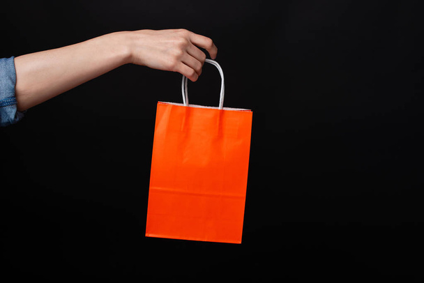 Frau hält orangefarbene Einkaufstasche über schwarzem Hintergrund - Foto, Bild