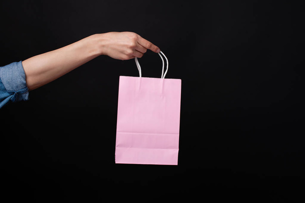 Frau hält rosa Einkaufstasche über schwarzem Hintergrund - Foto, Bild