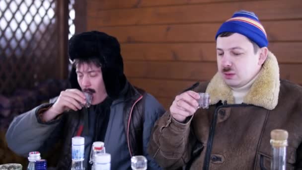 En la aldea dos amigos divertidos en ropa de invierno se sientan alrededor de la mesa con comida y hablar
 - Imágenes, Vídeo