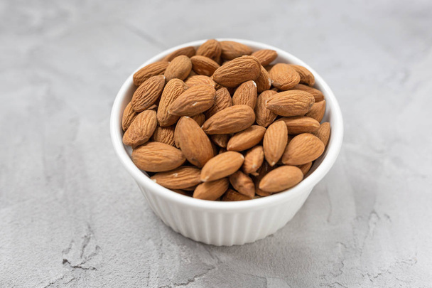 Raw almonds in a porcelain bowl on a gray background - Photo, Image