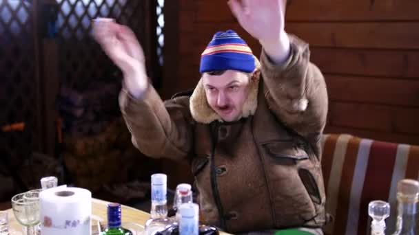 Älterer lustiger Betrunkener mit Schnurrbart in blauem Hut und Mantel tanzt hinter Tisch - Filmmaterial, Video