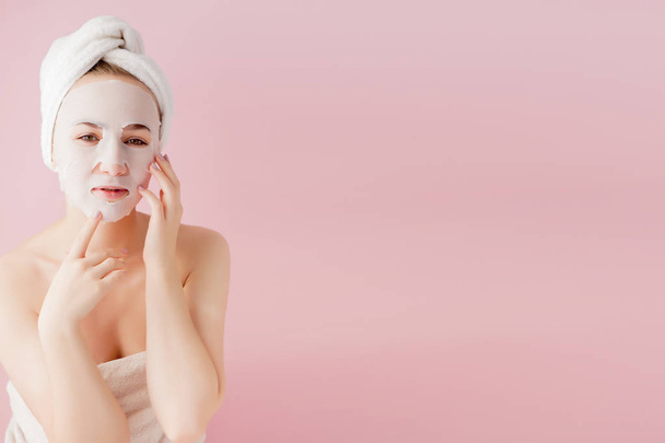 Beautiful young woman is applying a cosmetic tissue mask on a fa - Photo, Image