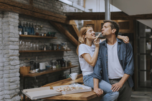 Jeune couple amoureux manger de la pizza pour le cou dans la maison rustique
 - Photo, image