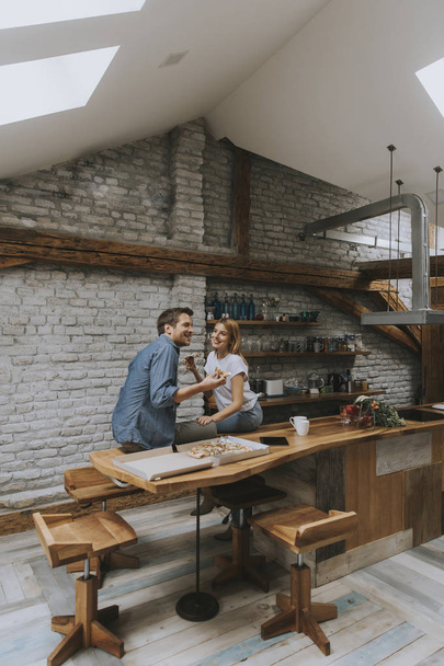 junges verliebtes Paar isst Pizza für den Hals in der rustikalen Wohnung - Foto, Bild