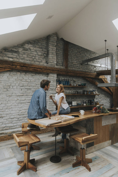 Jovem casal apaixonado comer pizza por sneck na casa rústica
 - Foto, Imagem