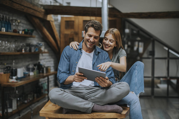 schönes junges Paar benutzt ein digitales Tablet und lächelt zu Hause in der Küche - Foto, Bild