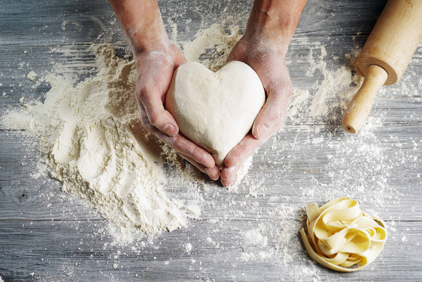 Masa en forma de corazón sostenida por las manos del panadero en primer plano
. - Foto, imagen