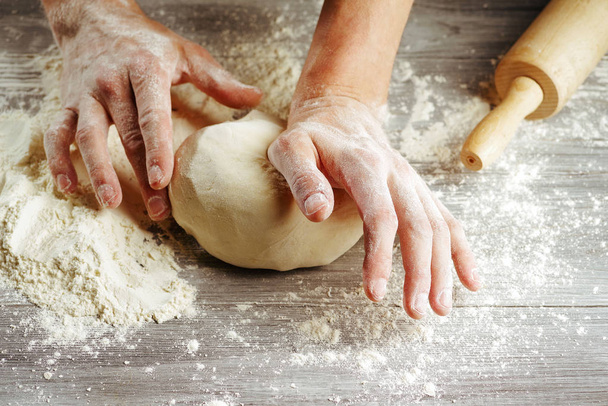 Hands in flour gently knead homemade dough close-up. - Photo, Image