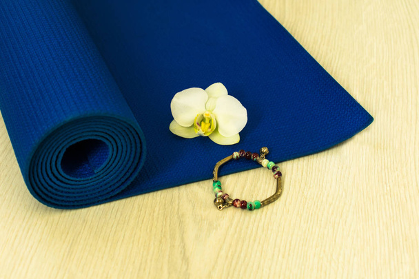 gerollte Yoga- oder Pilates-Matte für Bewegung auf natürlichem Holzboden, Sport, Nahaufnahme, weiße Blütenorchidee - Foto, Bild