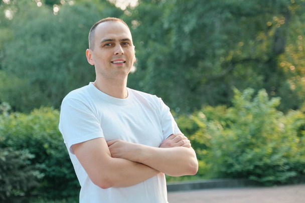 Outdoor portrait of confident smiling middle-aged sports man. Positive handsome male with arms crossed in white t-shirt looking at the camera - Foto, imagen