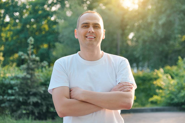 Outdoor portrait of confident smiling middle-aged sports man. Positive handsome male with arms crossed in white t-shirt looking at the camera - Foto, immagini