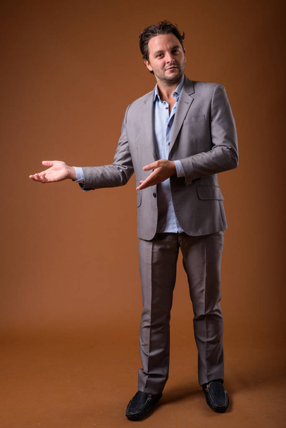 Studio shot of Italian businessman wearing suit against brown background - Fotografie, Obrázek