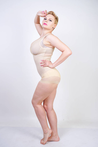 cute chubby girl with short hair and a curvy figure dressed in beige tight shapewear on a white background in the Studio - Fotografie, Obrázek